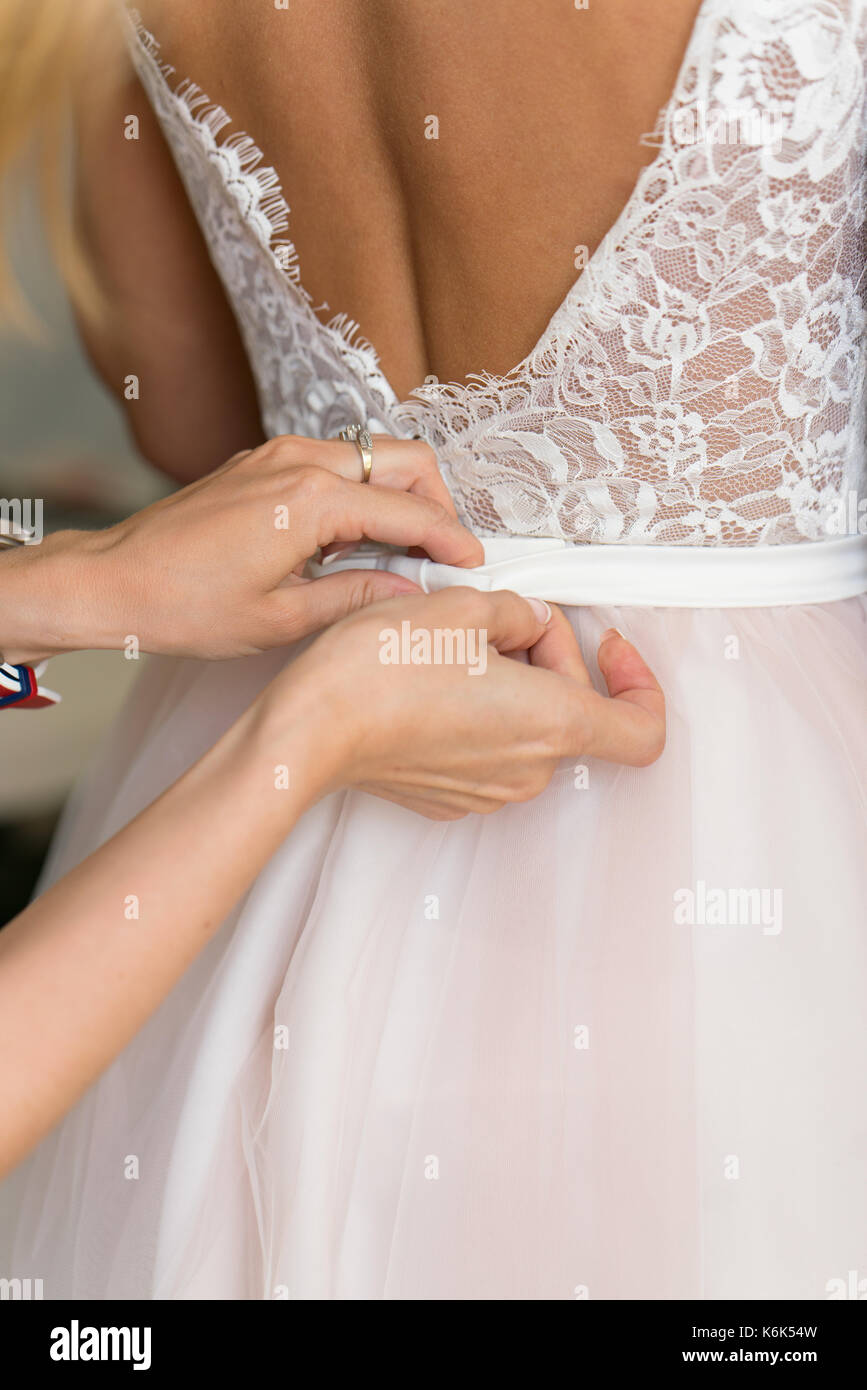 Hände der Brautjungfern, die Hilfe auf ein Kleid setzen Stockfoto