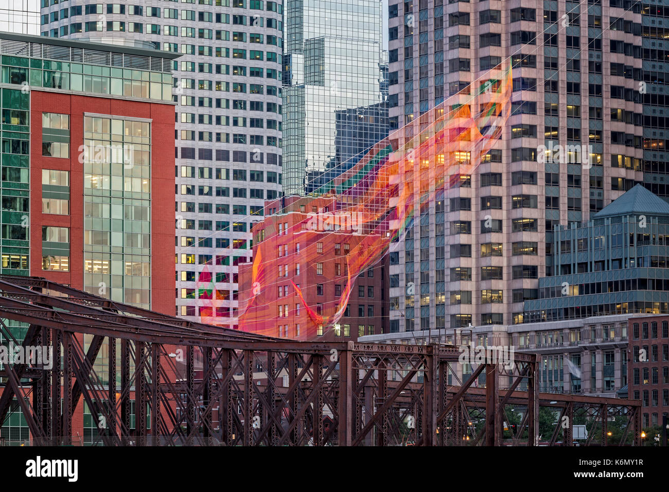 Bunte Fasern Über die Boston Skyline - Blick vom Hafen zu Fuß der Boston Skyline der Wolkenkratzer zusammen mit der bunten Janet Echelman", als ob es Schon hier "aerial Skulptur über Boston's Rose Kennedy Greenway ausgesetzt. Die Skulptur ist von Hand gefertigt - spleißen Seil und verknoten Garn in einer vernetzten Mesh von mehr als einer halben Million Teilnehmern. Wenn eines ihrer Elemente bewegt, jedes andere Element ist betroffen. Auch im Vordergrund zu sehen, ist der alte nördliche Brücke. Stockfoto