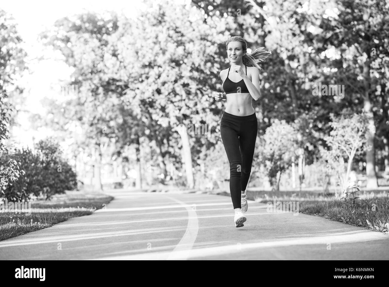Schwarzweiß-Aufnahme einer jungen schönen weiblichen Athleten genießen, laufen im Wald Lächeln weg schauen copyspace Positivität aktiven Lebensstil passen Ton Stockfoto