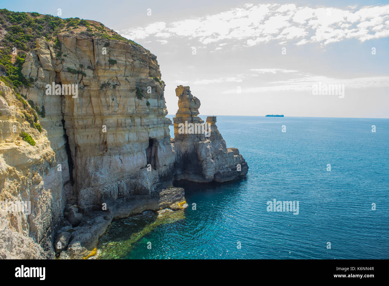 Maltesische cliff, cliff Erosion: wellenschnitt Plattform, Meer Höhle und Stacks. Nachweis von Cliff Rezession. Ein Handelsschiff auf dem Horizont. Stockfoto