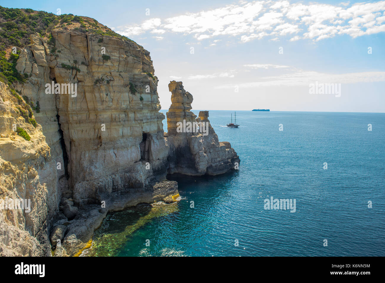 Maltesische cliff, cliff Erosion: wellenschnitt Plattform, Meer Höhle und Stacks. Nachweis von Cliff Rezession. Ein Handelsschiff auf dem Horizont und einer Yacht. Stockfoto
