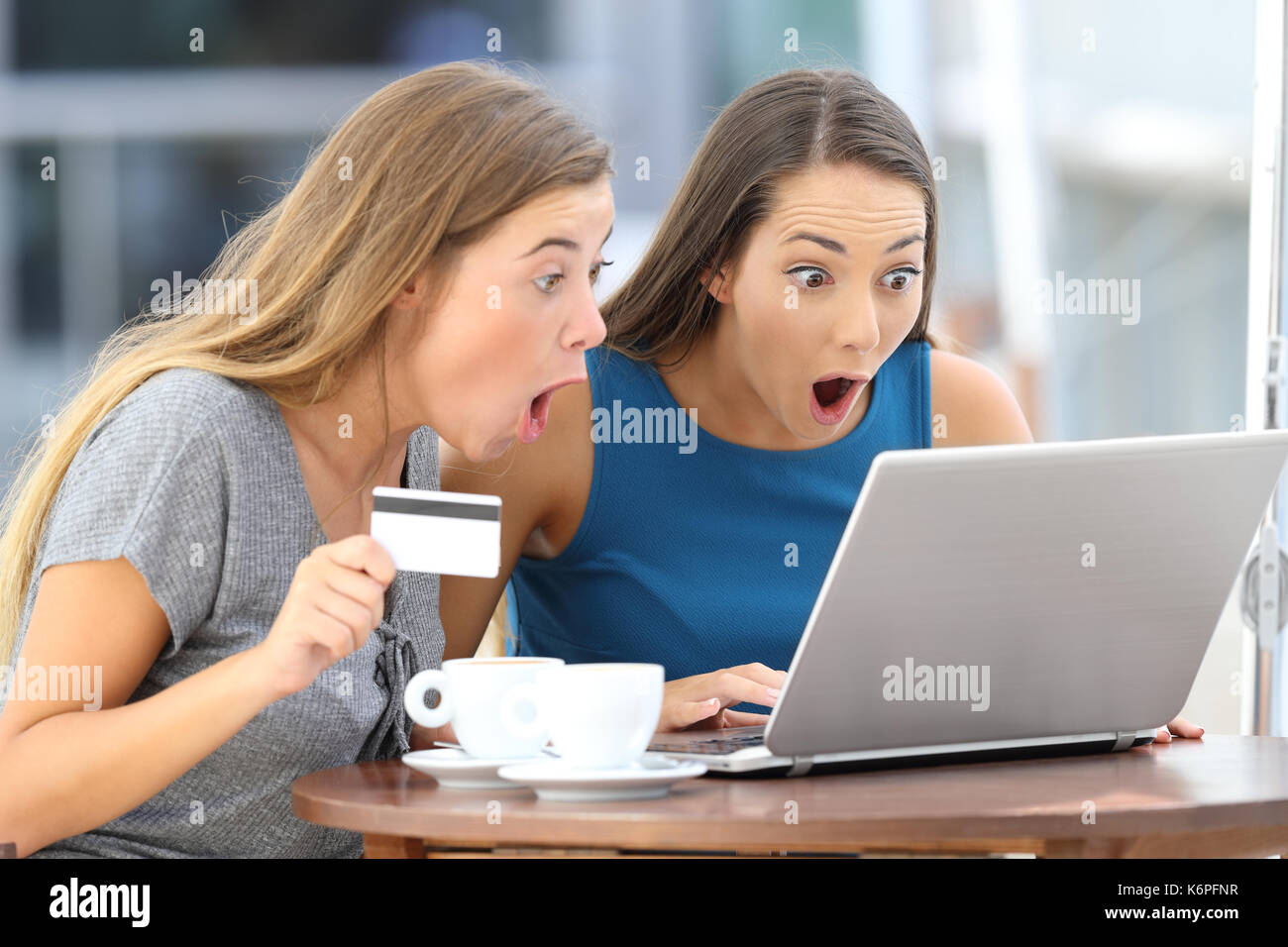 Zwei erstaunt Freunde Kaufen auf Linie mit einem Laptop und der Kreditkarte in einer Bar auf der Terrasse sitzen Stockfoto