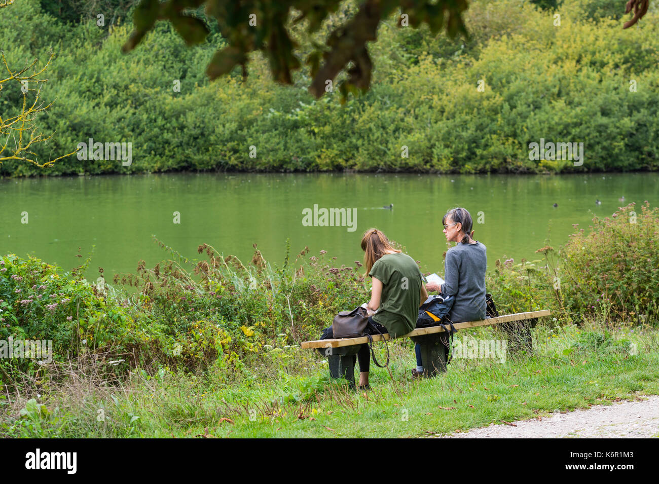 Mutter und Tochter sitzen zusammen an einem See im frühen Herbst in Großbritannien. Stockfoto