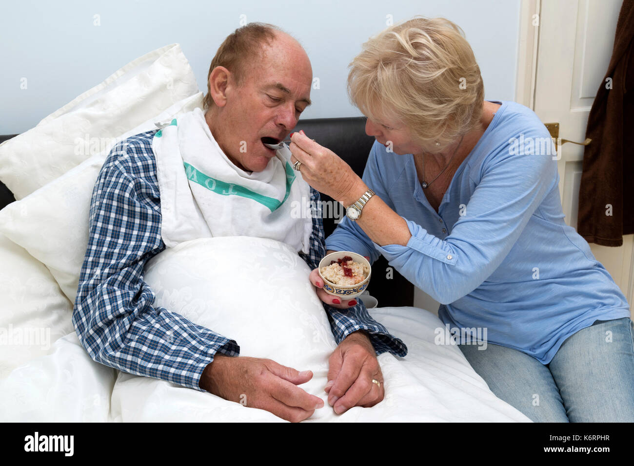 Eine ältere kranke bettlägerigen Mann Frühstück gespeist durch seine Frau und seine Helfer, Stockfoto