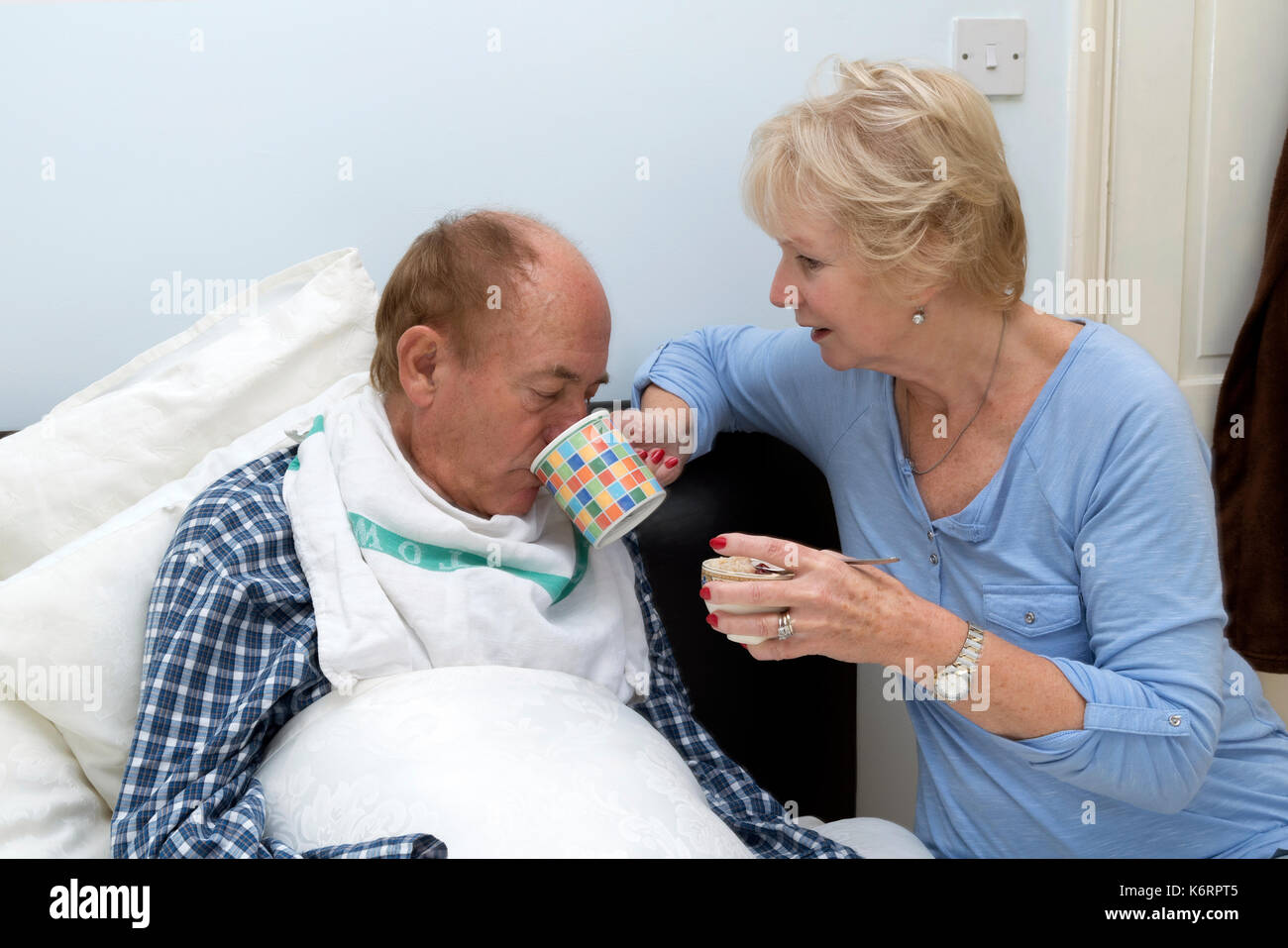 Älterer bettlägeriger Mann, der von seiner Pfänderin und seiner Frau einen Drink erhalten hat Stockfoto