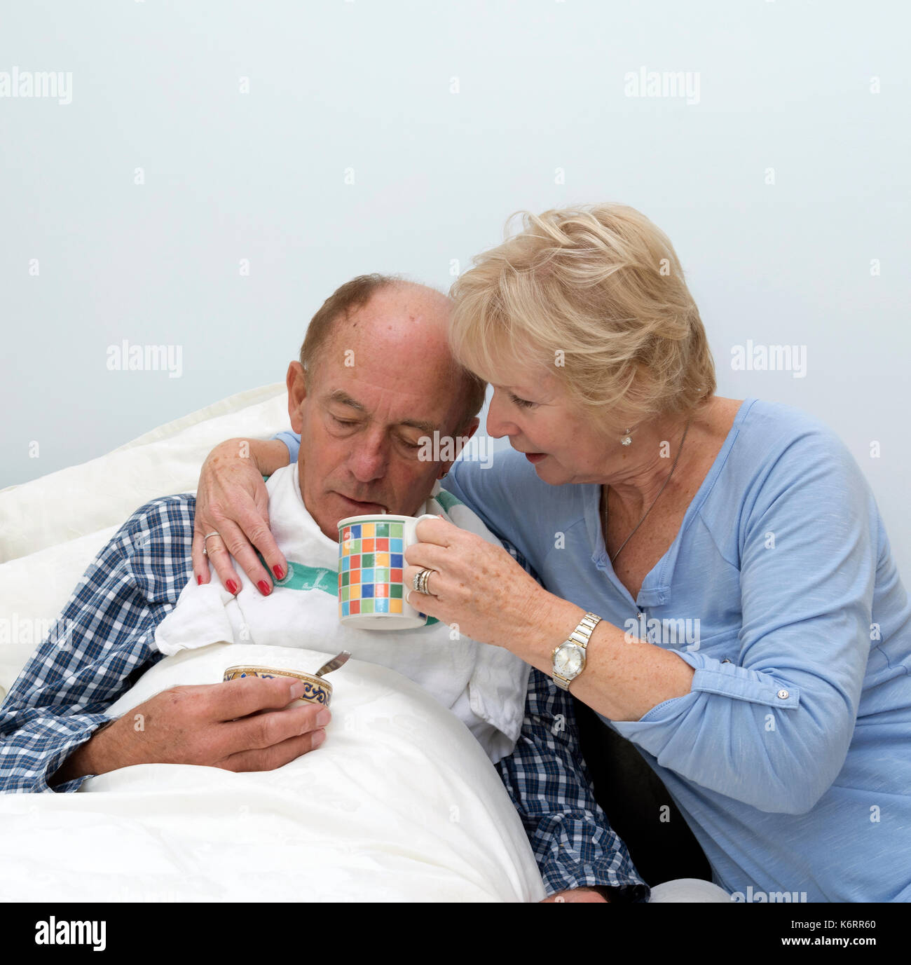 Älterer bettlägeriger Mann, der von seiner Pfänderin und seiner Frau einen Drink erhalten hat Stockfoto