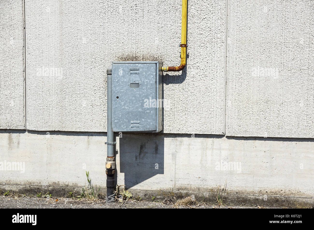 Alte wasser Metallrohre mit Halterungen vor einem Putz an der Wand mit Metall Box für Wasserzähler festgesetzt. Stockfoto