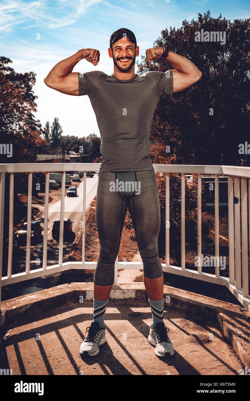 Junge, urbane, lächelnden Sportler zeigt seine Muskeln nach dem Training an der Brücke und auf Kamera. Stockfoto