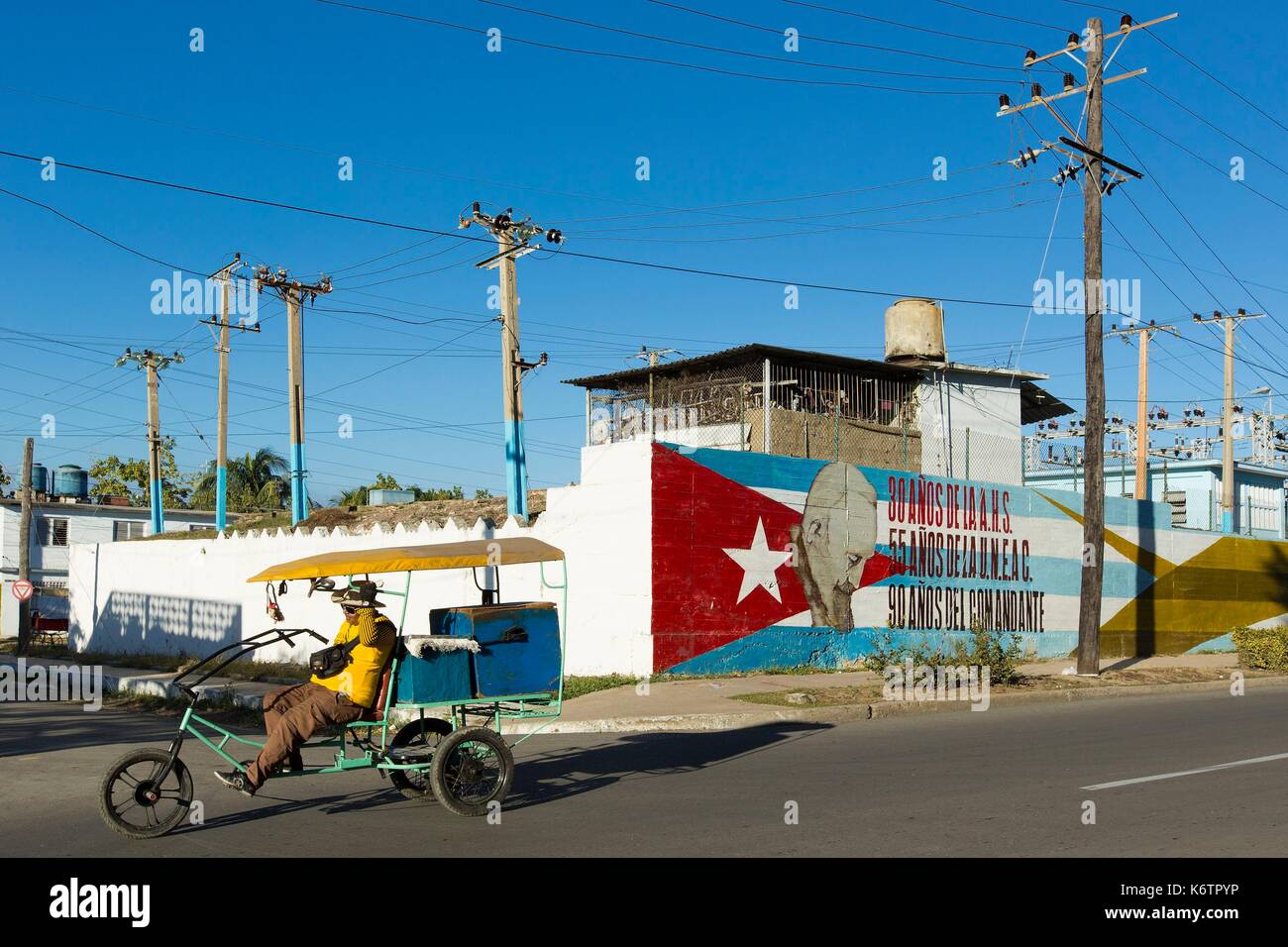 Cuba, Cienfuegos Provinz, Cienfuegos, Rikscha bicitaxi vor einem Wandbild, das die kubanische Flagge und Fidel Castro Stockfoto