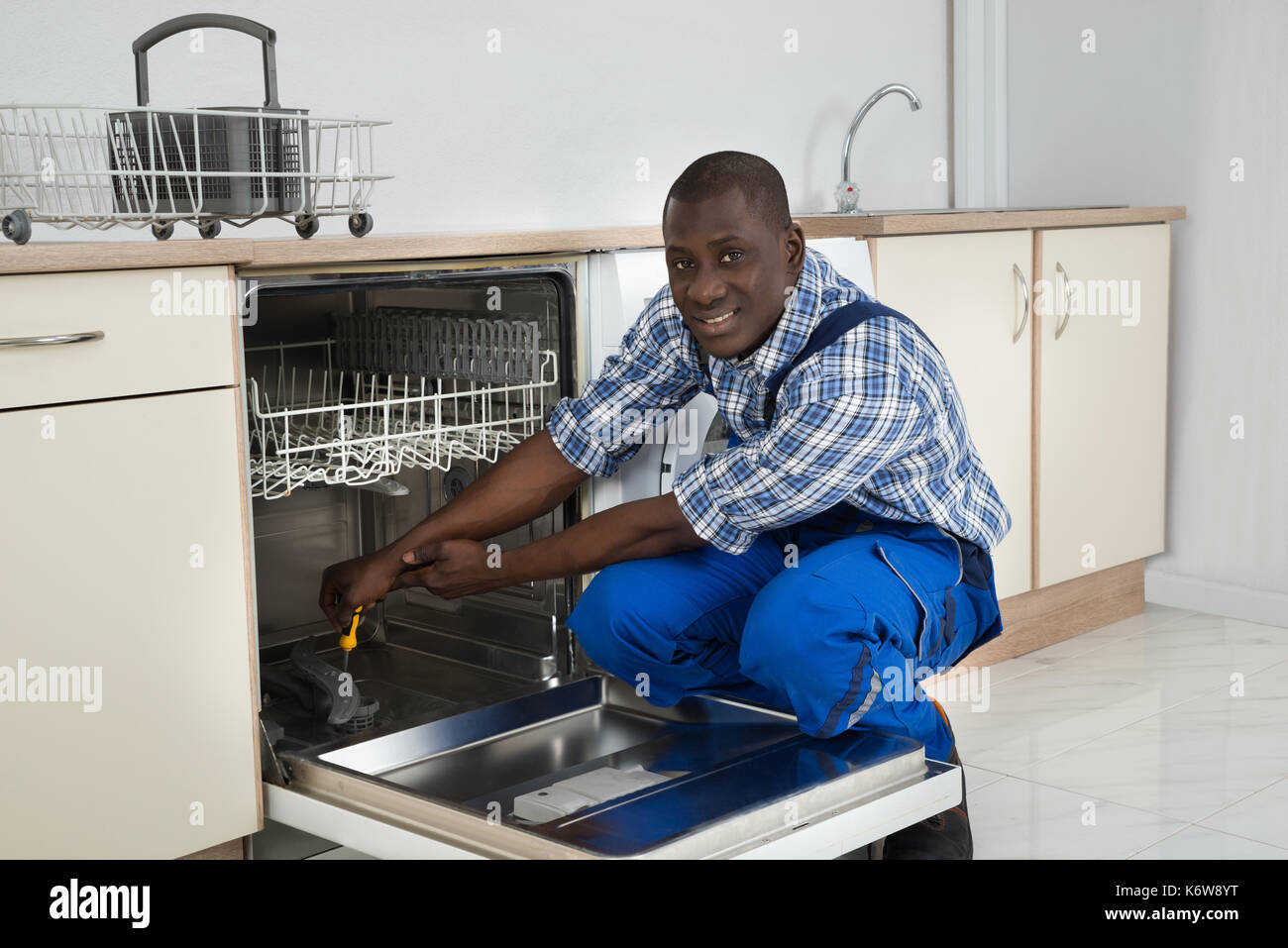 Junge Glücklich afrikanische Techniker Reparatur Geschirrspüler mit Schraubendreher in der Küche Stockfoto