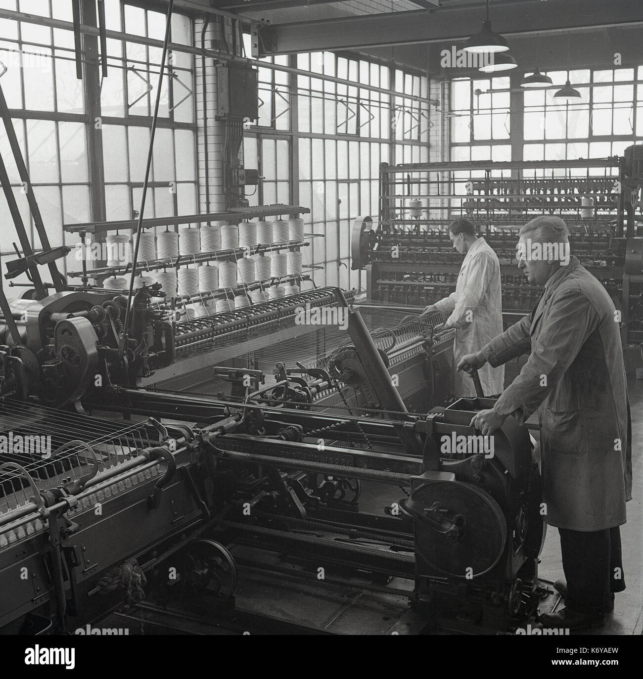 1950, historische, Bild zeigt Männer in Latzhosen arbeitenden großen komplexen mechanischen Maschinen, ein Spinner und Spinning Mule in der kammgarn Spinningraum, Leeds, England, UK. Kammgarn ist eine feine glatte Stoff aus langen Fasern der Wolle Garn und der spining Prozess langsamer ist. Stockfoto