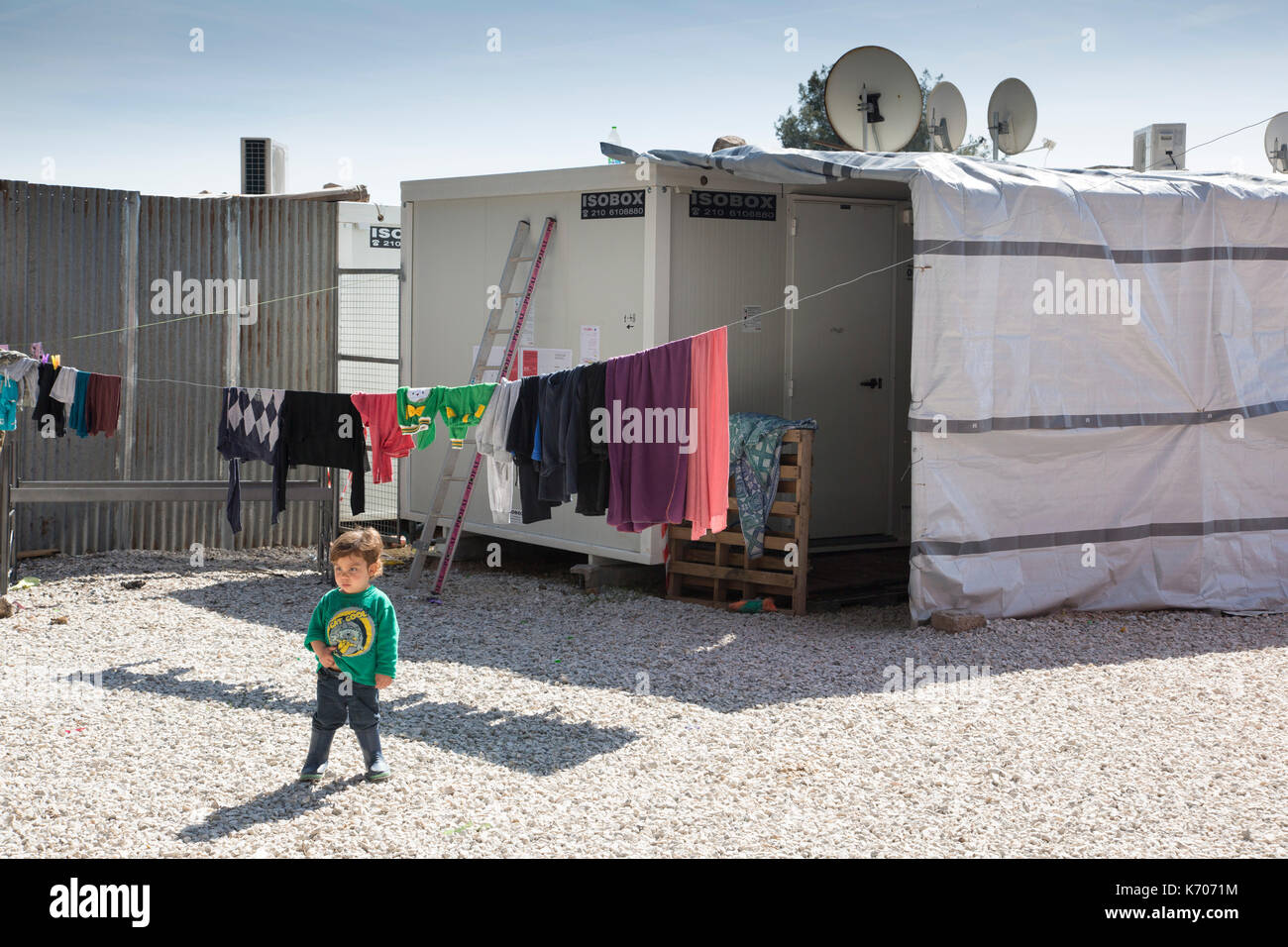 Auf dem Kies zwischen vorgefertigten Einheiten, in denen Flüchtlinge aus Syrien untergebracht sind, untersucht ein einjähriges Kind das Flüchtlingslager Ritsona. Stockfoto