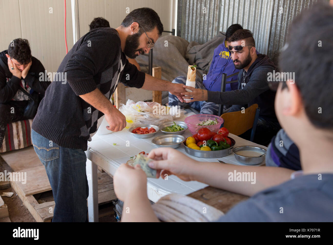Ein improvisiertes Restaurant im Flüchtlingslager Ritsona in Griechenland. Der Gastronom überreicht einem Gast eine Packung, während ein Junge mit Geld in der Hand wartet. Stockfoto