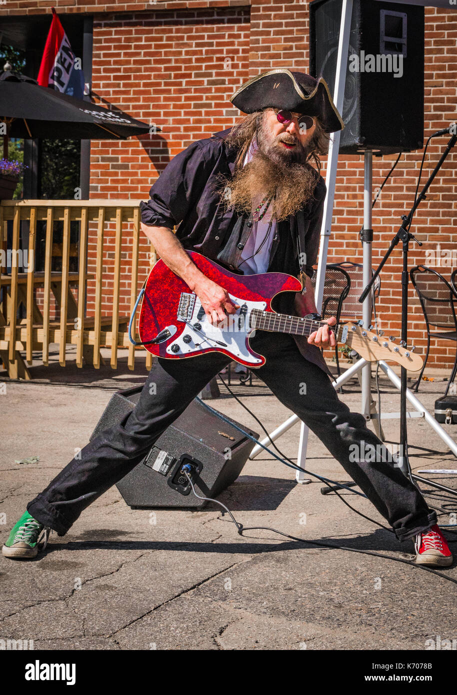 Ein Kaukasier Männlich rock guitar Interpret in einem schwarzen Hemd und Piraten Hut singt in einem lokalen outdoor Music Festival in Keene, NH. Stockfoto