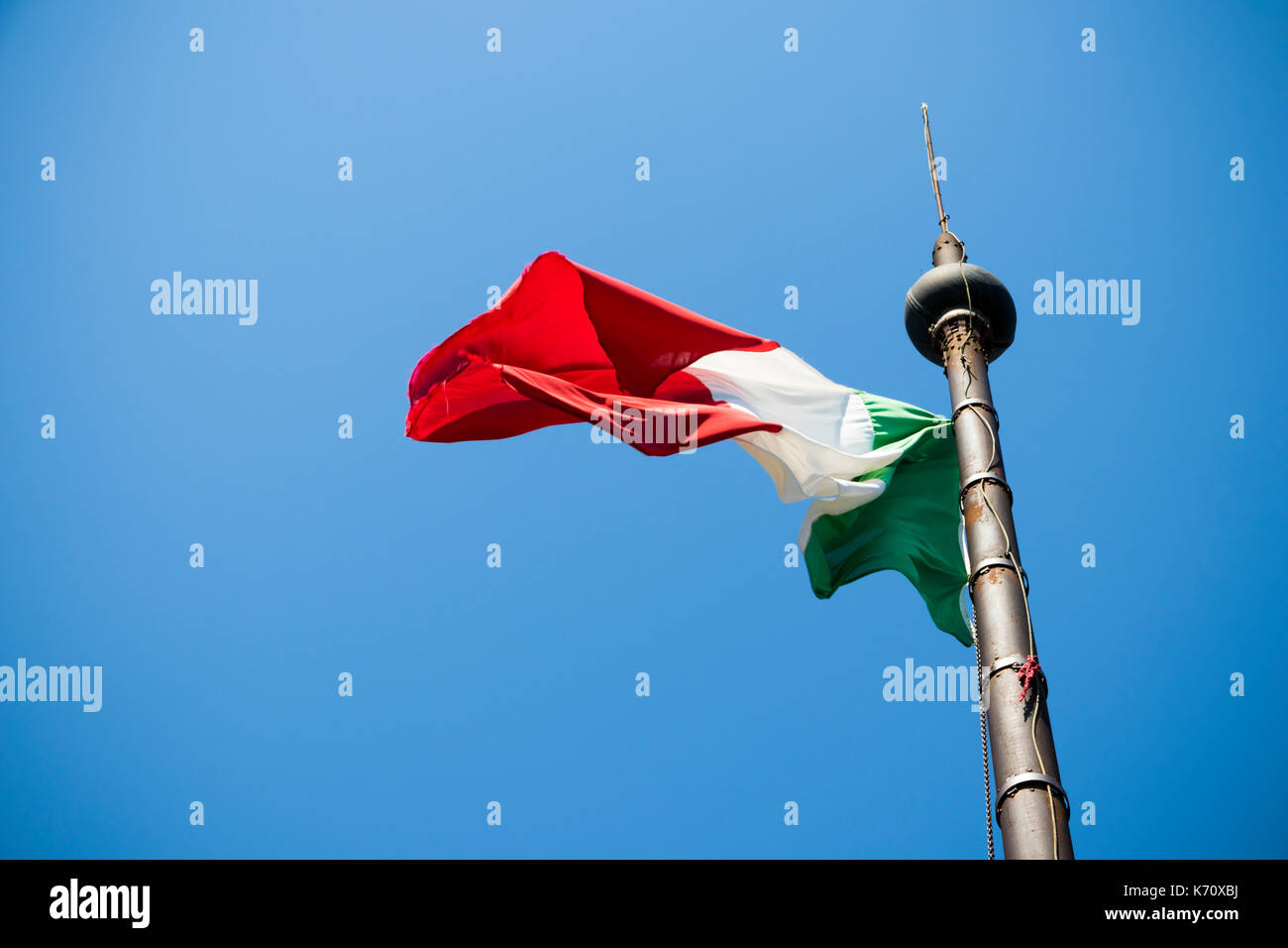 Eine wehende Flagge von Italien, auch als il tricolore bekannt, auf einem Mast über einen blauen Himmel Hintergrund Stockfoto