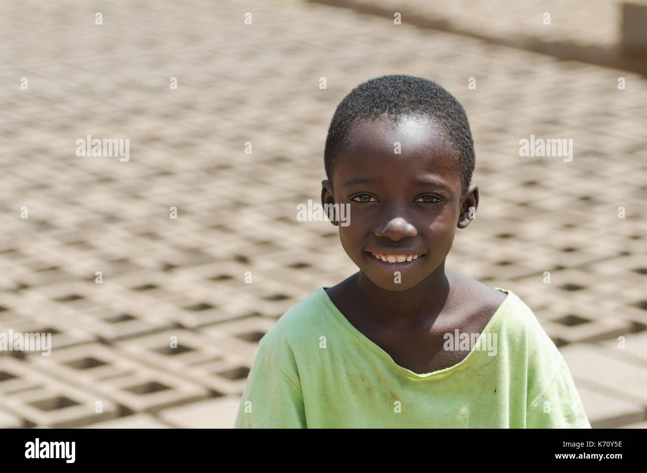 Kleines afrikanisches Kind lächelnd im Freien hinter Steine - Kinderarbeit Konzept Stockfoto