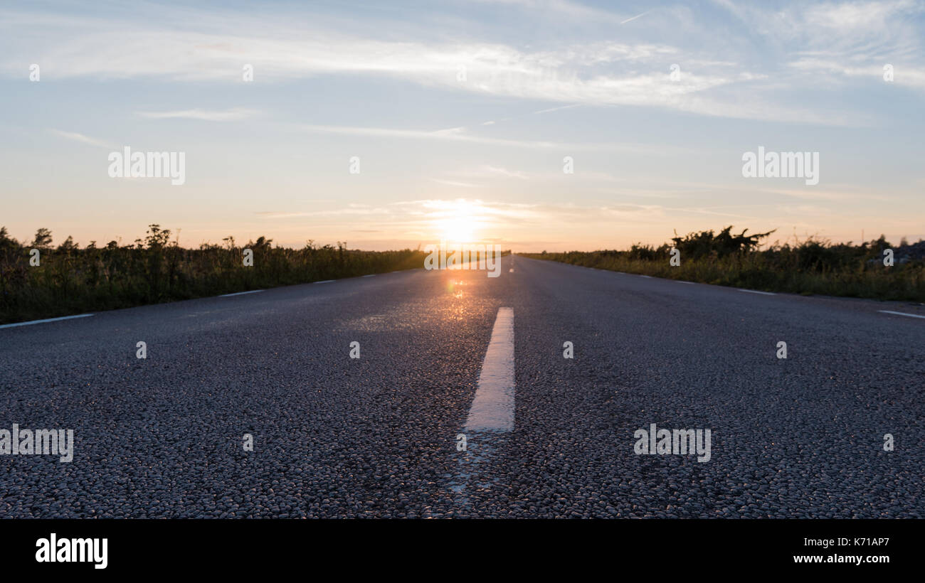 Extreme Low Angle View auf eine asphaltierte Straße geradeaus durch Sonnenuntergang Stockfoto