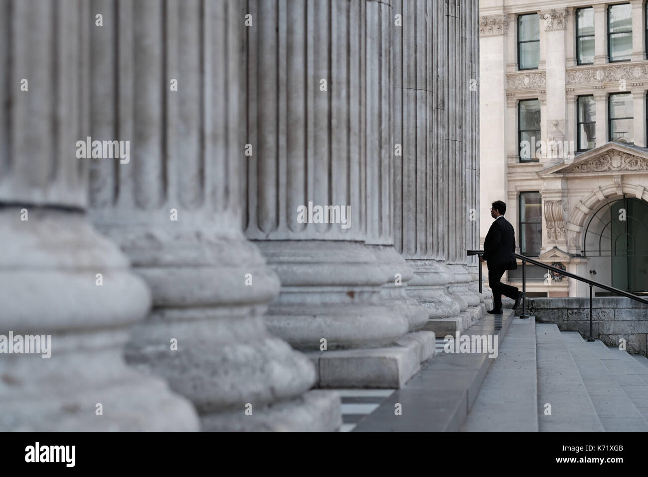 Mann in einem schwarzen Anzug zu Fuß die Treppe hinauf und durch die West Front Kolonnade in die Saint Paul's Cathedral, London, UK Stockfoto