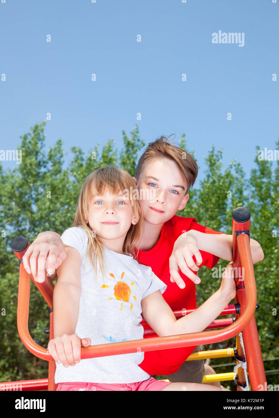 Low Angle View von Bruder und Schwester auf einem Klettergerüst im Sommer Spielplatz am Kamera Suche posing Stockfoto