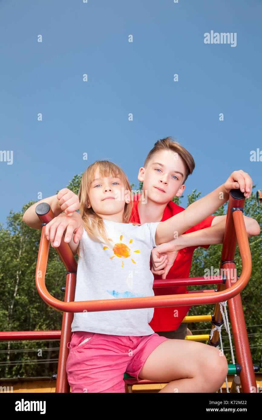 Low Angle View von Bruder und Schwester auf einem Klettergerüst im Sommer Spielplatz am Kamera Suche posing Stockfoto