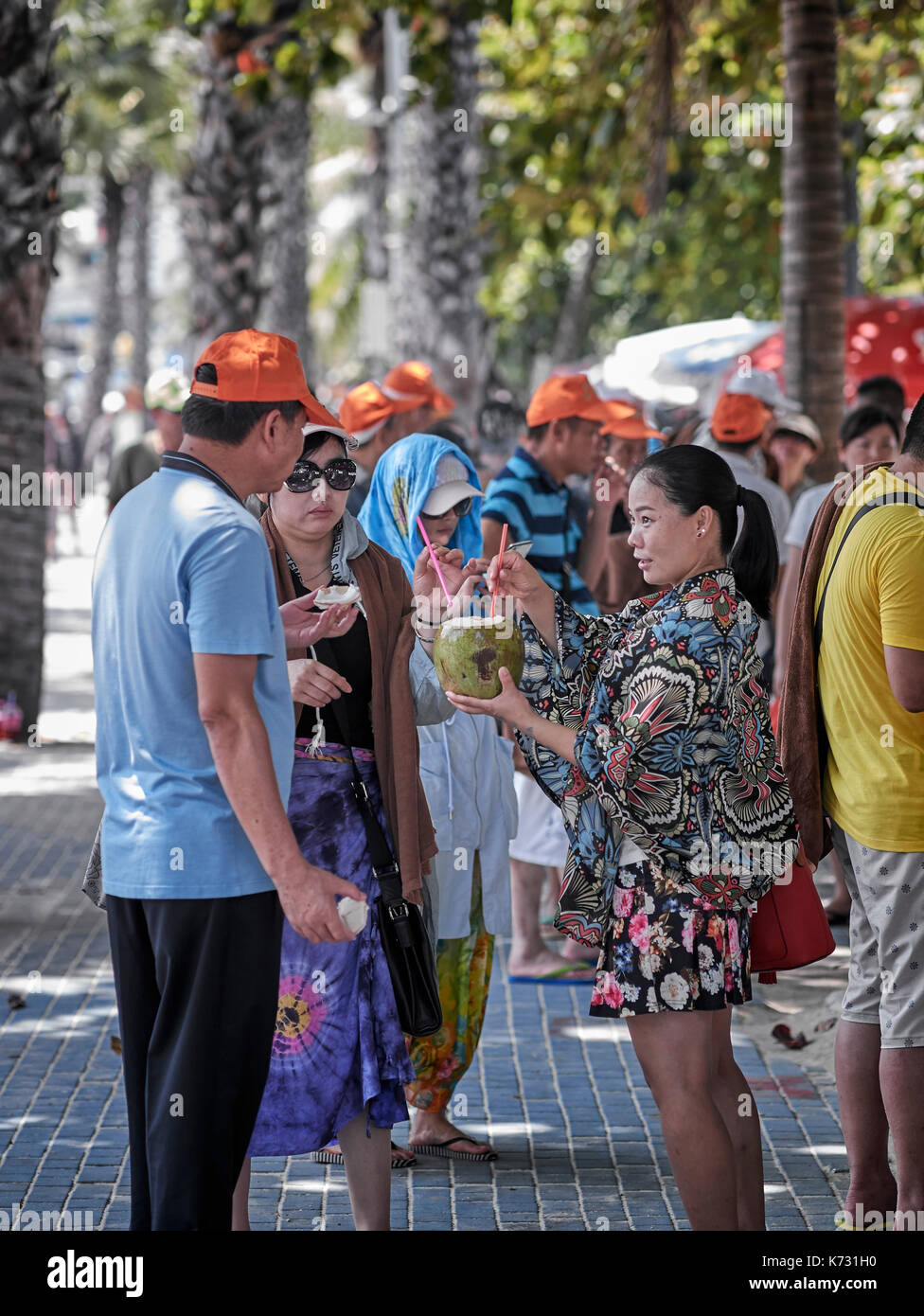 Chinesische Touristen teilen sich einen Kokosnuss-Drink in Pattaya Thailand Südostasien. Chinesische Touristengruppe. Pattaya Beach Road Stockfoto