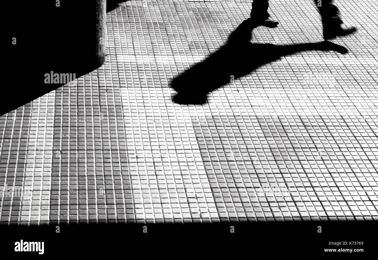 Unscharfe Silhouette der Beine und Schatten einer Person zu Fuß auf eine Stadt Bürgersteig in Schwarz und Weiß mit hohem Kontrast Stockfoto