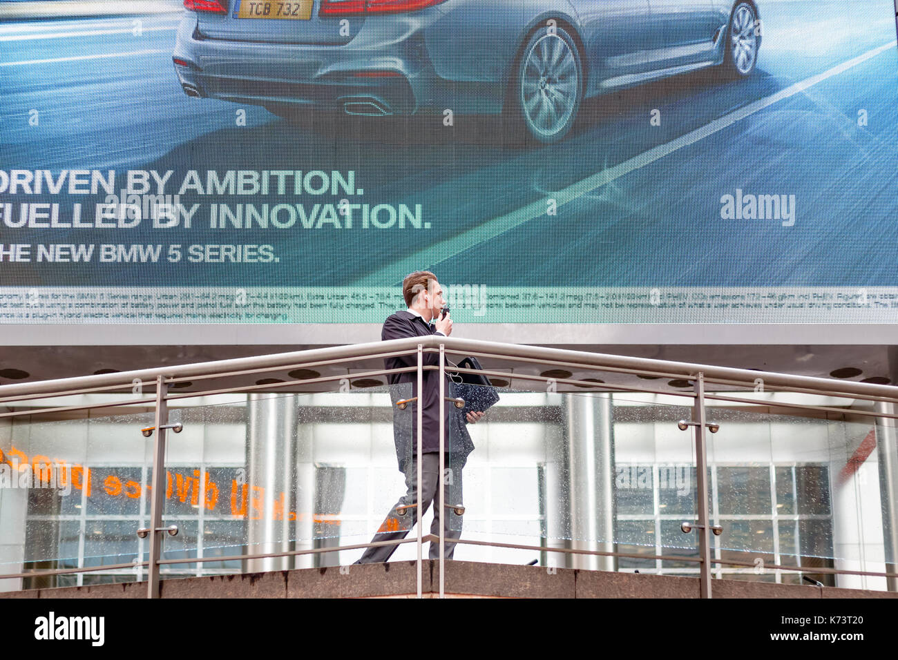 London, Großbritannien - 15 September, 2017 - Auto commercial auf einen Bildschirm in Canary Wharf mit ein büroangestellter vor ihm stehend angezeigt Stockfoto