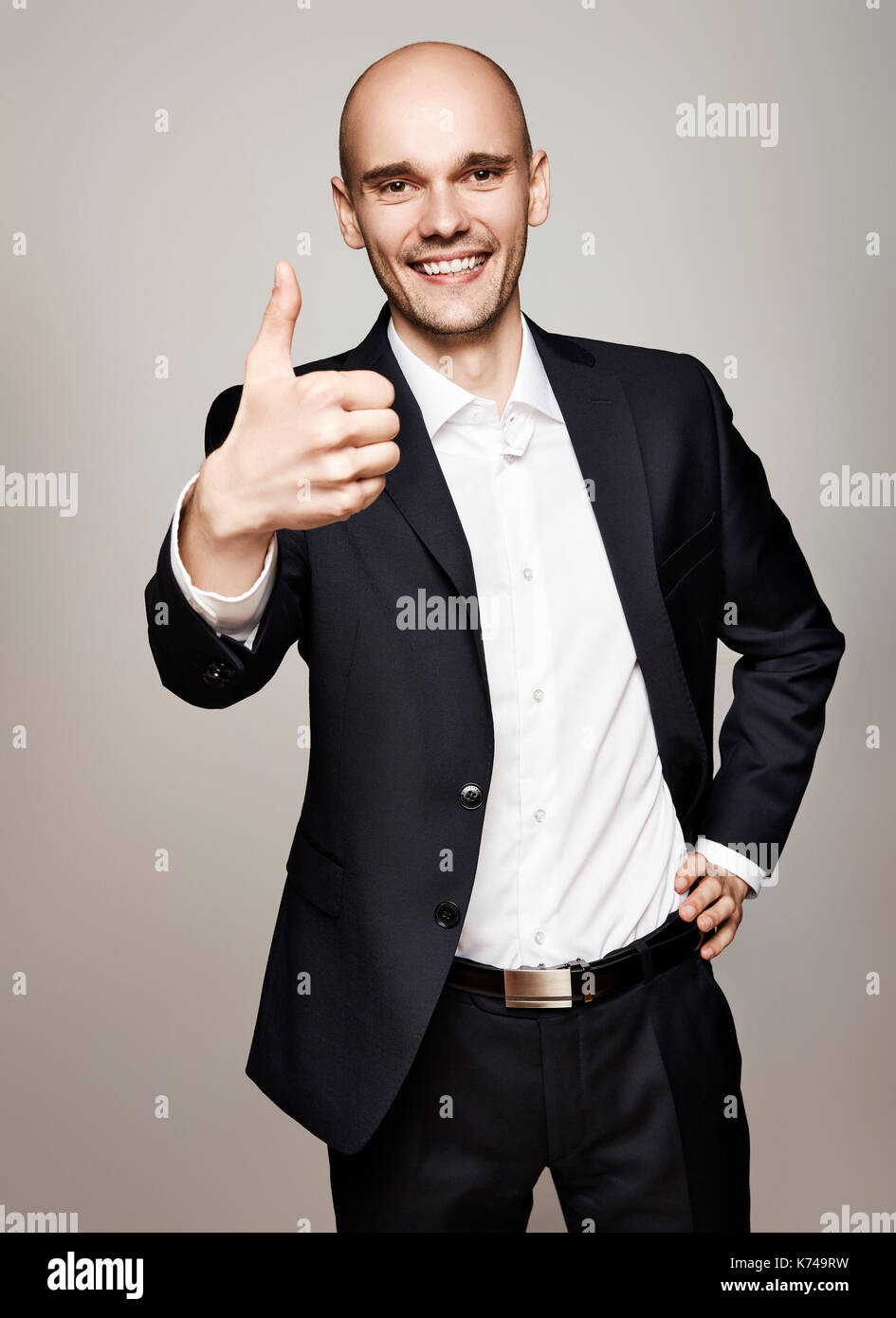 Glückliche junge Geschäftsmann zeigt seinen Daumen. Studio shot auf grauem Hintergrund. Stockfoto