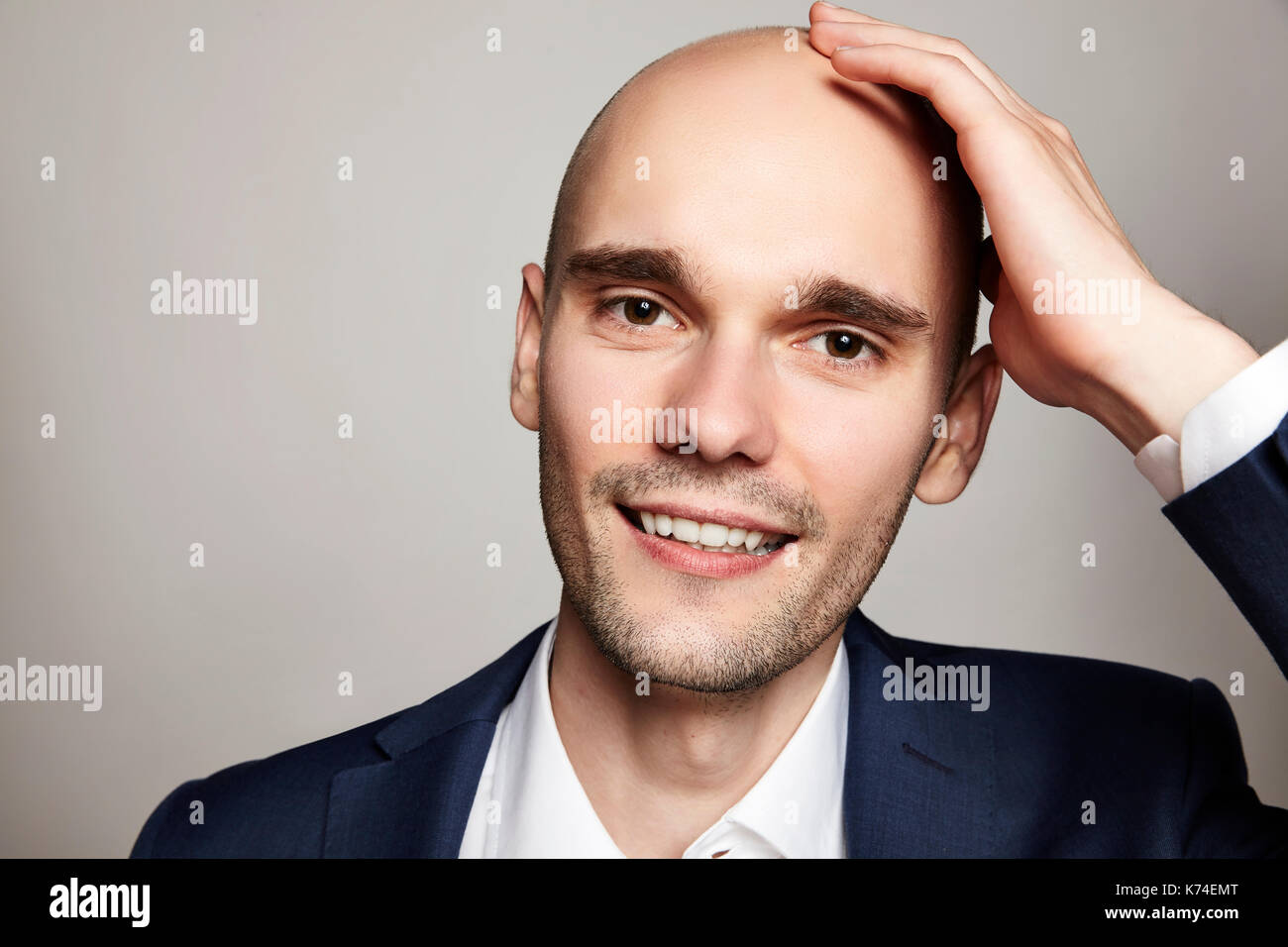 Nahaufnahme Porträt einer stattlichen glatzköpfige Mann seinen Kopf streicheln. Er lächelt. Grauer Hintergrund. Horizontale. Stockfoto