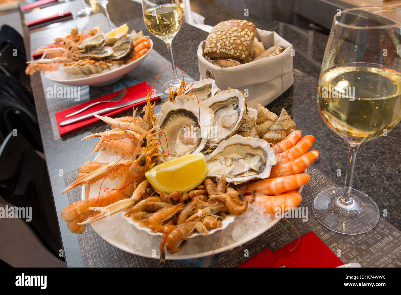 Platte mit Meeresfrüchten: Austern, Jumbo, Garnelen, Garnelen, Wellhornschnecken und Glas Weißwein Stockfoto