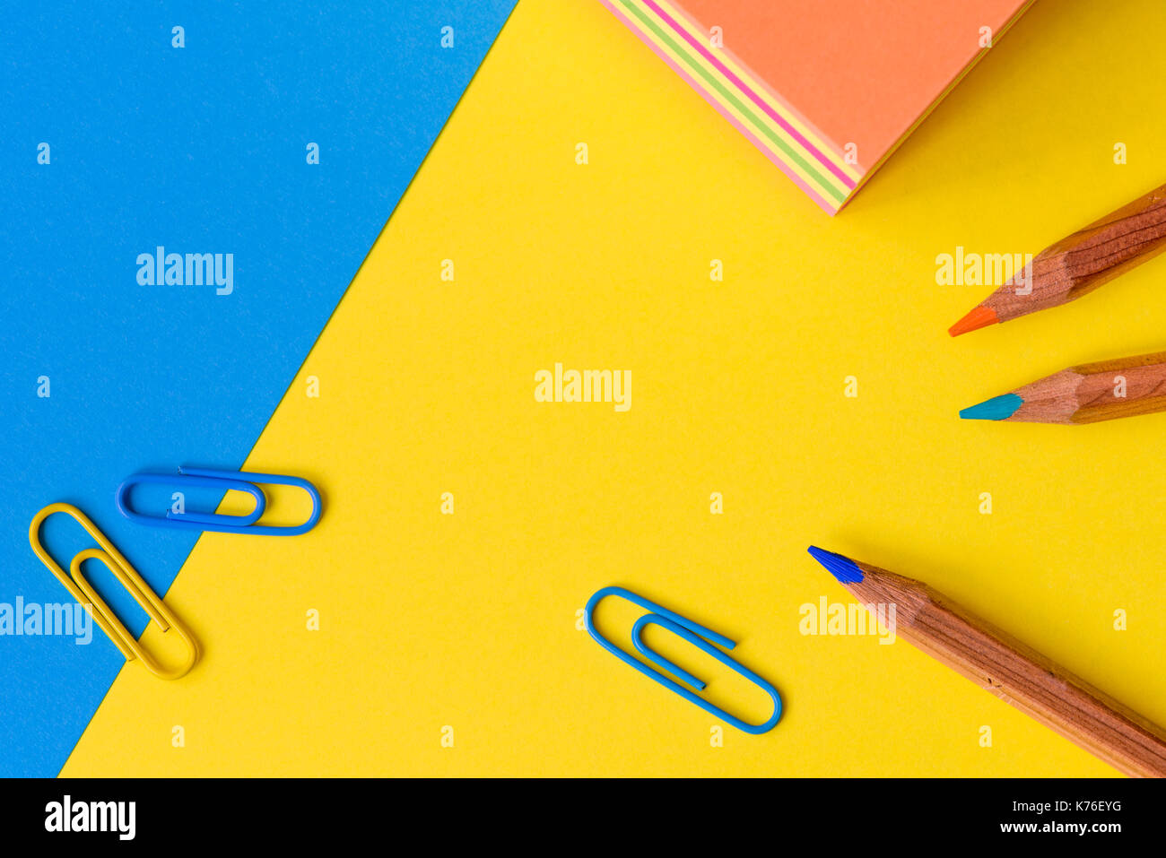 Eine bunte Büro oder Geschäft Konzept mit Büroklammern, Stifte und Memo Block gegen einen blauen und gelben Hintergrund und kopieren Raum isoliert. Stockfoto
