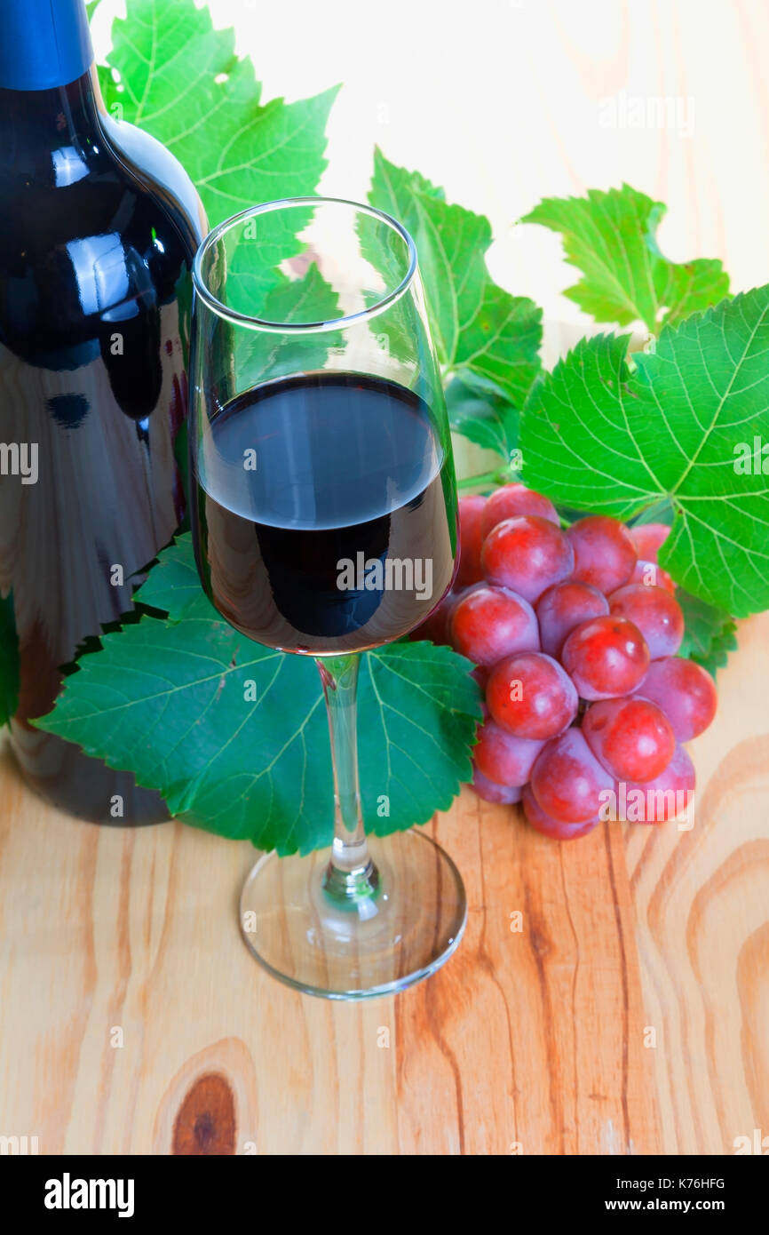 Flasche Rotwein mit Glas und Trauben auf Holz. Stockfoto