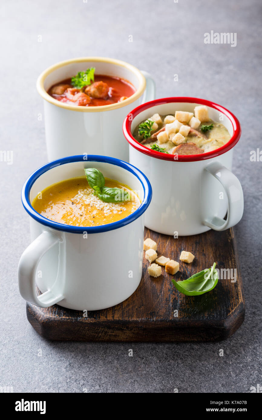 Verschiedene köstliche hausgemachte Suppen in Emaille Becher mit Zutaten. Gesunde Ernährung Konzept. Stockfoto