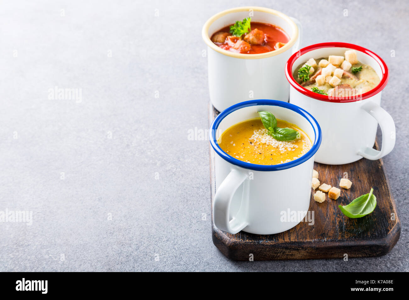 Verschiedene köstliche hausgemachte Suppen in Emaille Becher mit Zutaten. Gesunde Ernährung Konzept mit kopieren. Stockfoto