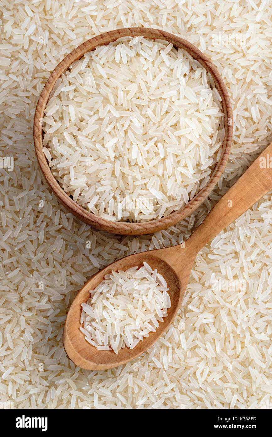Hölzerne Schüssel und Löffel mit parboiled Reis auf dem Hintergrund der zerstreuten Reis. Ansicht von oben. Produkt mit hoher Auflösung Stockfoto