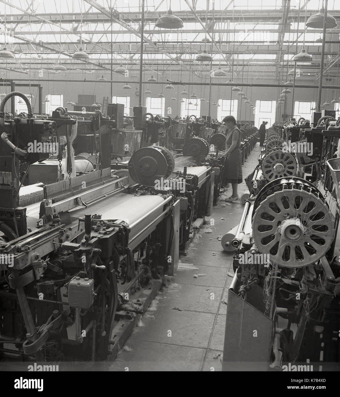 In den 1950er Jahren standen historische Arbeiterinnen auf Holzdielen mit mechanisierten Leinenwebstühlen in einer großen Textilfabrik in Nordirland. Stockfoto