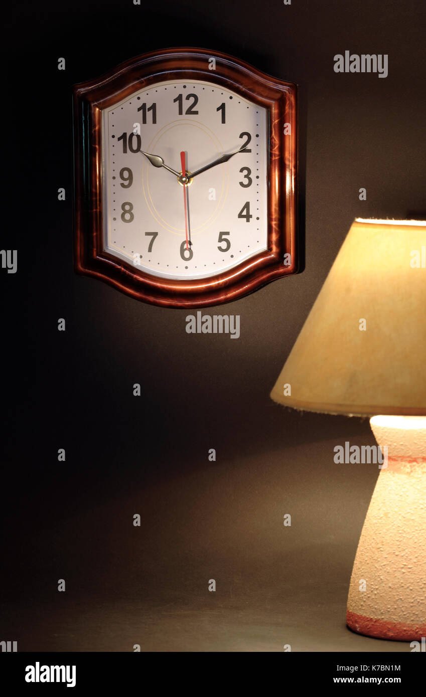 Stillleben mit leuchtenden Schreibtischlampe in der Nähe der Uhr auf dunklem Hintergrund Stockfoto