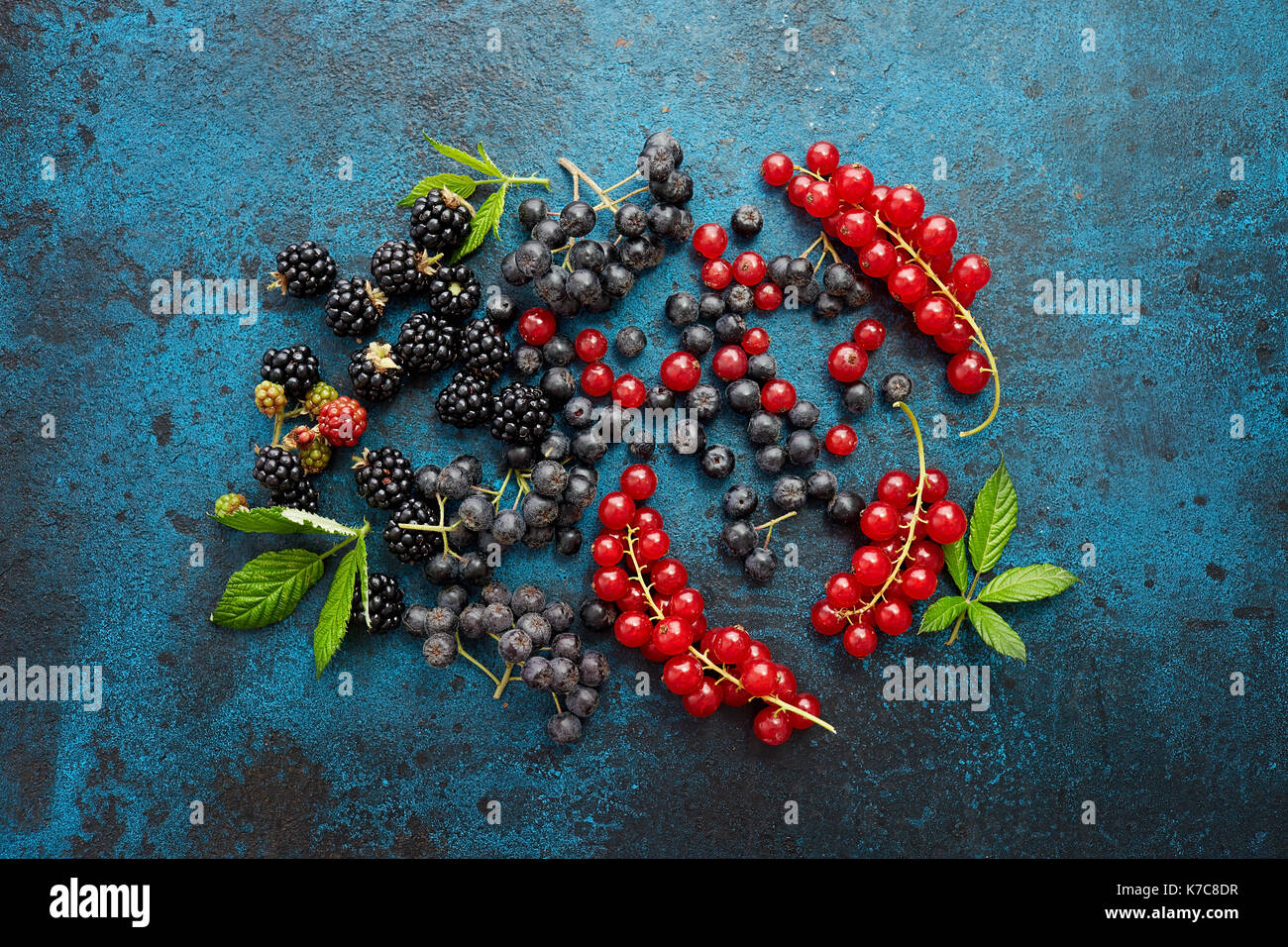 Verschiedene frische Beeren mit Blättern auf Metall Hintergrund. Mischung aus frischen Beeren mit Blättern auf strukturierte Metall Hintergrund. Stockfoto