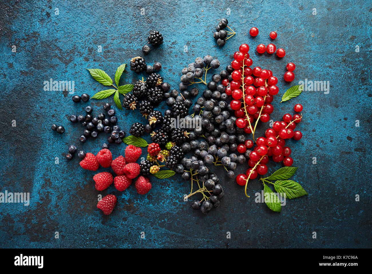 Verschiedene frische Beeren mit Blättern auf Metall Hintergrund. Mischung aus frischen Beeren mit Blättern auf strukturierte Metall Hintergrund. Stockfoto