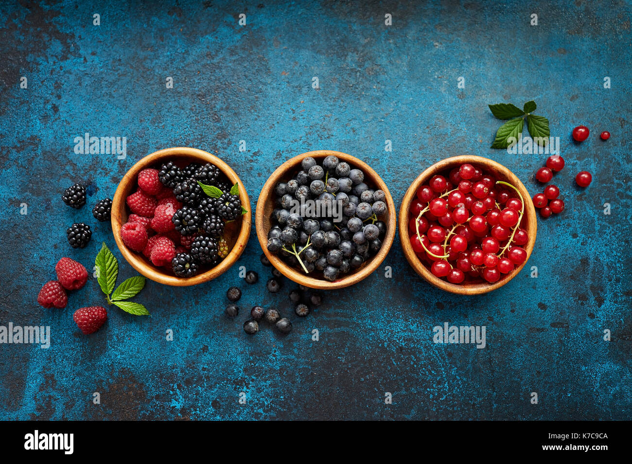 Verschiedene Sommer Früchte in einem hölzernen Schüsseln. Verschiedene frische Beeren mit Blättern auf Metall Hintergrund. Stockfoto