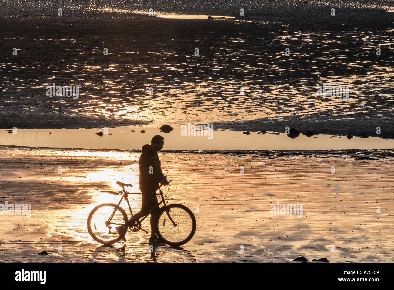 Ein einsamer Radfahrer hält am Strand, um den Sonnenuntergang zu bewundern. Stockfoto