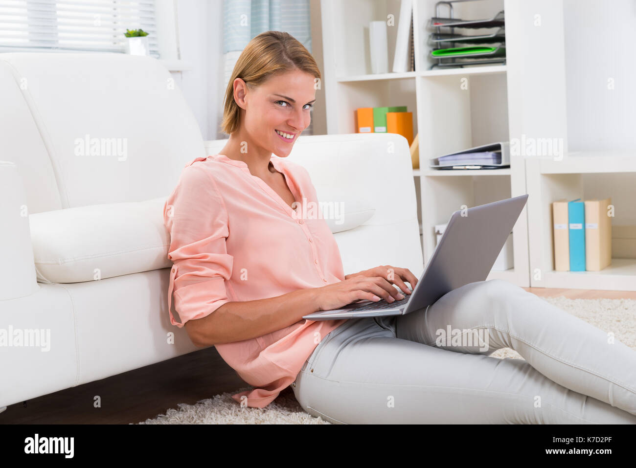 Junge Frau sitzt in der Nähe von dem Sofa auf Laptop eingeben Stockfoto