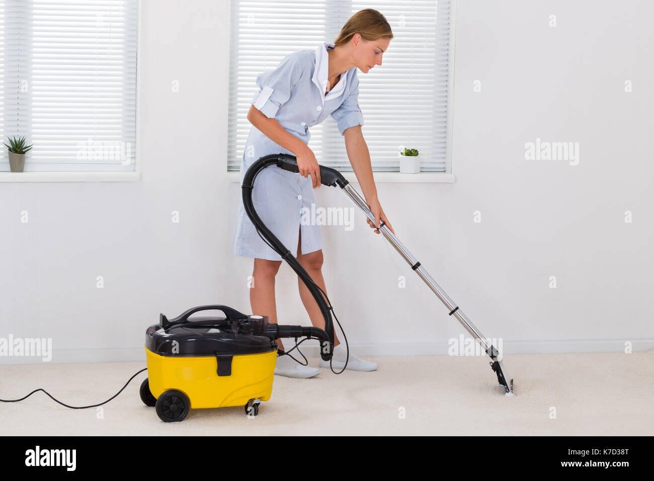 Junge weibliche Zimmermädchen Etage mit Staubsauger reinigen Stockfoto