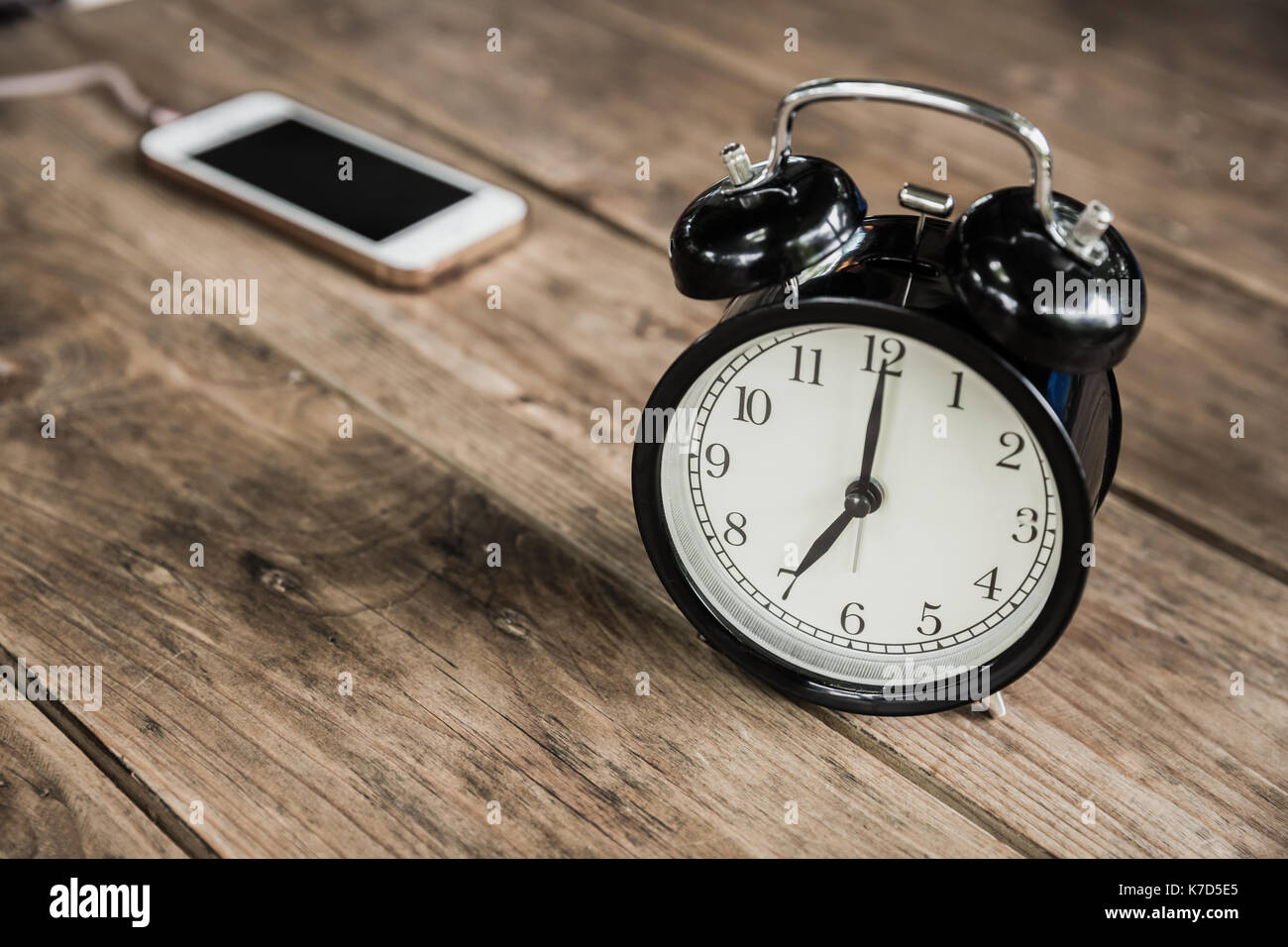 Uhrzeiten um 7 Uhr morgens auf Holz Tisch mit smart phone Aufladen im Cafe blur Hintergrund. Stockfoto