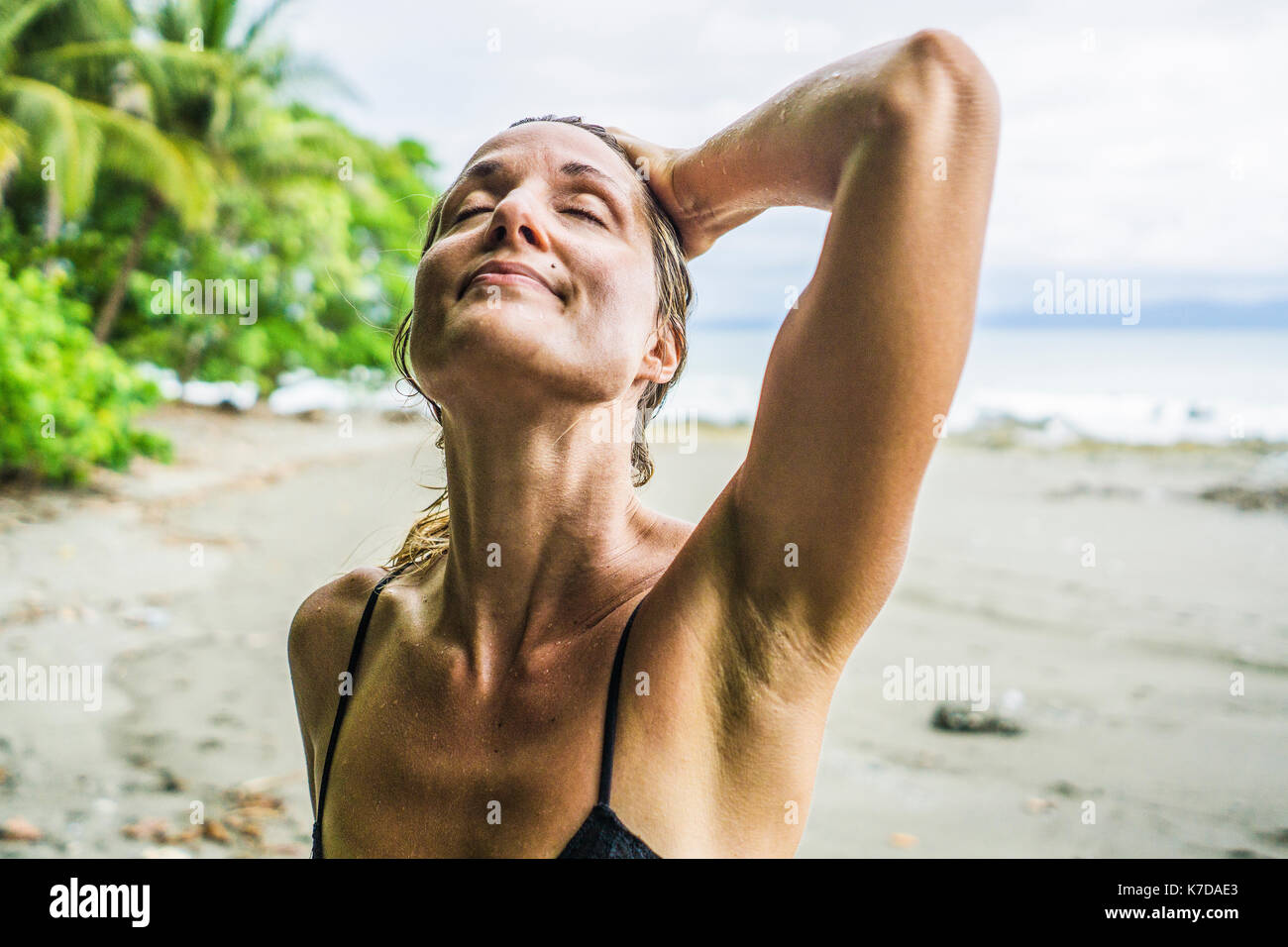 Entspannt Mitte der erwachsenen Frau stehend mit der Hand in das nasse Haar am Strand Stockfoto