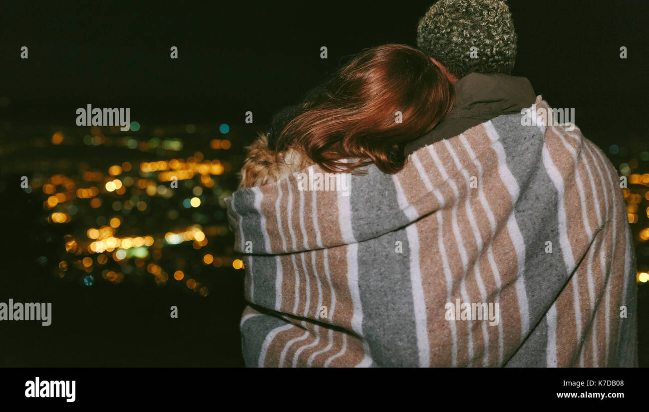 Ansicht der Rückseite des jungen Paares in einer Decke gegen Stadtbild bei Nacht gewickelt Stockfoto