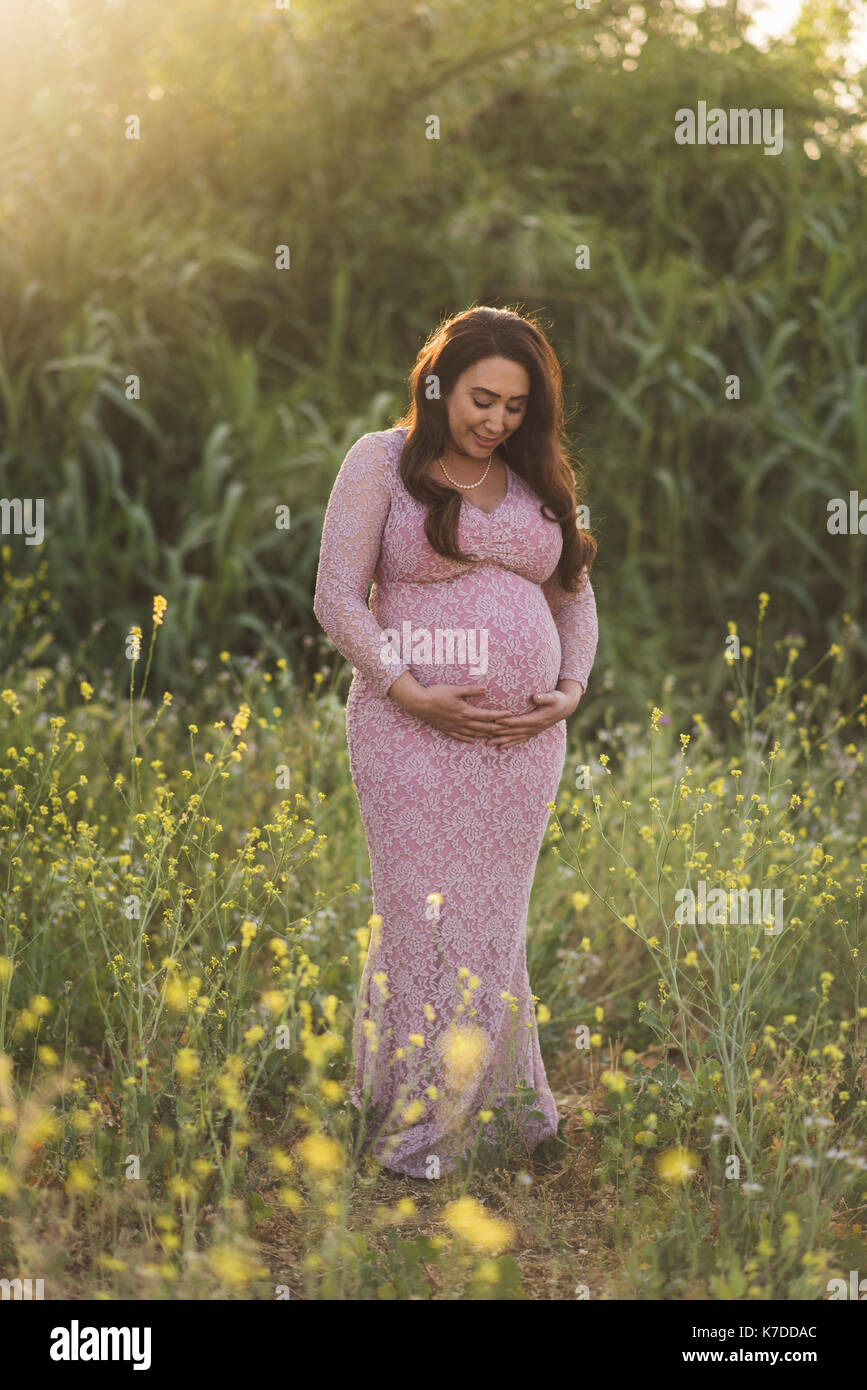 Schwangere Frau mit Hände auf Bauch stehend auf dem Feld im Park Stockfoto