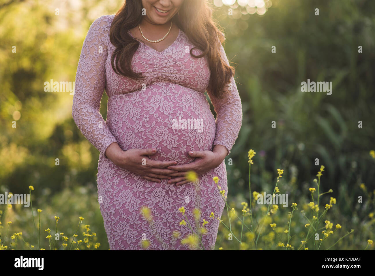 Mittelteil der schwangeren Frau mit Hände auf Bauch stehend auf dem Feld im Park Stockfoto