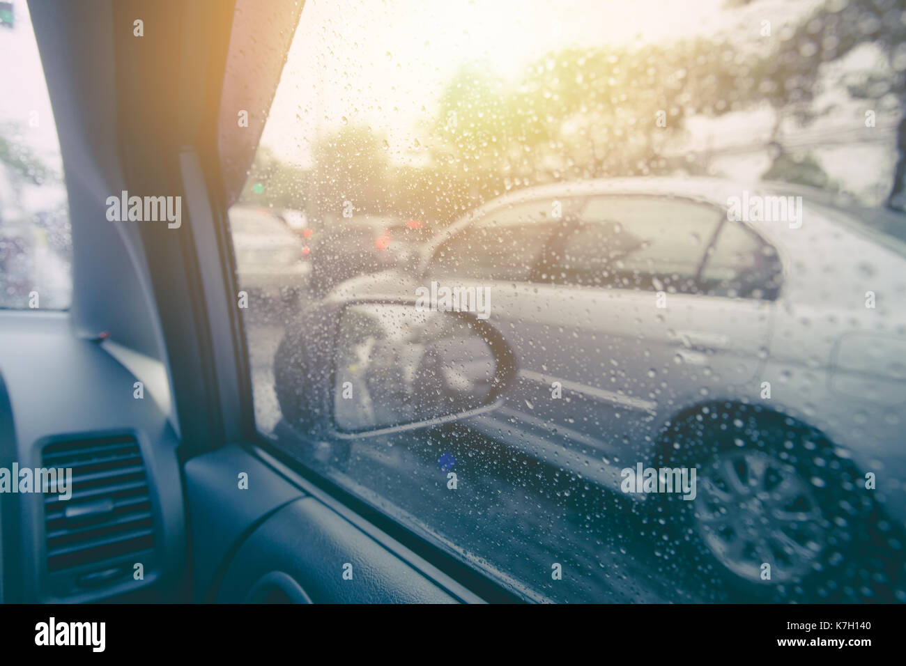 Auto fahren in Regenzeit. Fahrzeug Seitenfenster mit regen Tropfen Wasser und Sonne Hintergrund. Stockfoto