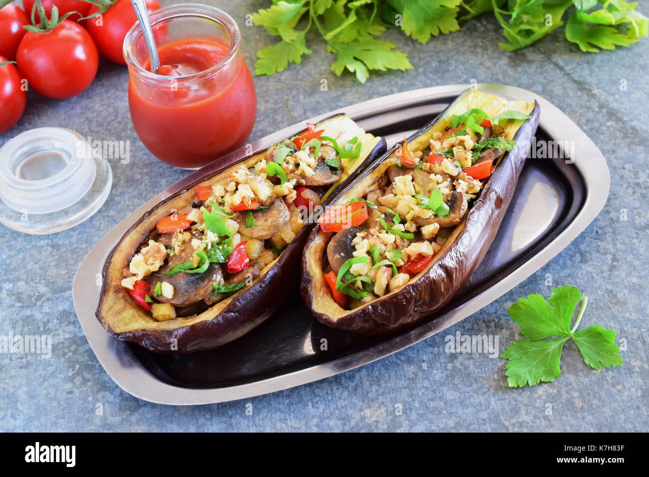 Auberginen gefüllt mit Pilzen, Zwiebeln, Karotten, Tomaten und die Muttern auf eine Metallplatte auf grauem Hintergrund. Vegetarisches Essen. gesunde Ernährung Konzept. Stockfoto